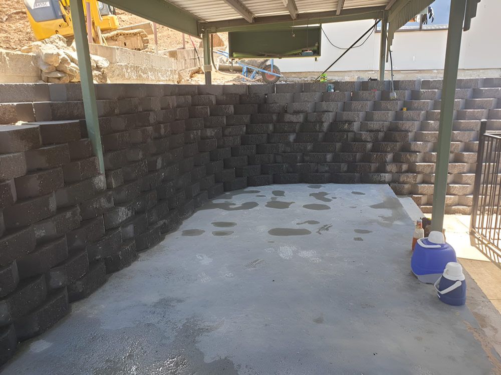 A Brick Wall Is Being Built Next To A Concrete Floor — Austen Landscaping & Earthmoving in Deeragun, QLD