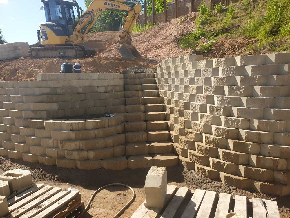 Brick Retaining Wall Construction with an Excavator Positioned on the Top — Austen Landscaping & Earthmoving in Ingham, QLD