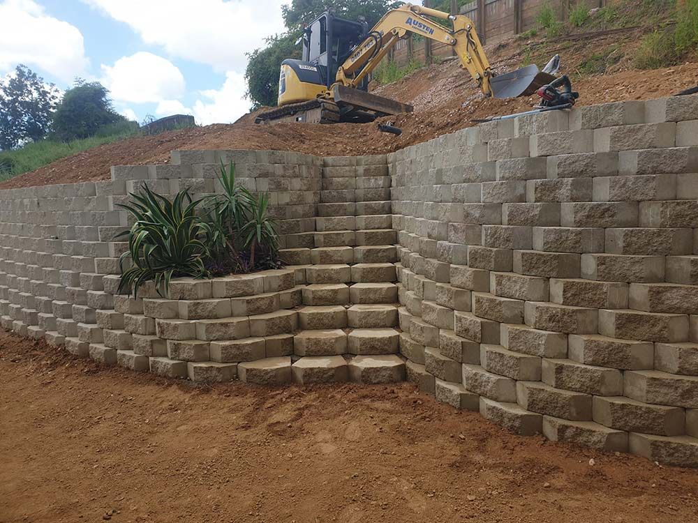 A Concrete Retaining Wall Featuring Integrated Stairs With An Excavator — Austen Landscaping & Earthmoving in Deeragun, QLD