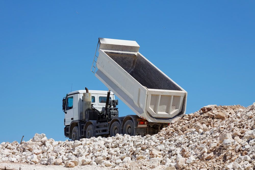 A White Truck Is Dumping Rocks Into A Pile Of Rocks — Austen Landscaping & Earthmoving in Ayr, QLD