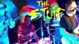 Band performing on a colorful stage with blue and pink lights, “The Stuffs” sign behind them
