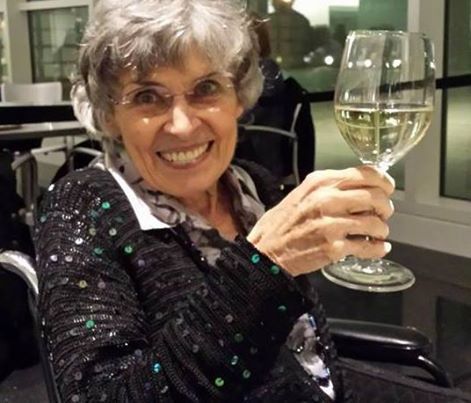 Smiling woman in a black sequined top raises a wine glass at a table
