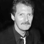 Black-and-white portrait of a man with a mustache and suit, facing the camera with a slight smile.