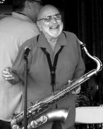 Smiling man holding a saxophone at a performance, with a microphone nearby