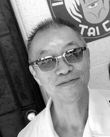 Man wearing sunglasses and a white collared shirt, posing indoors near a wall sign.