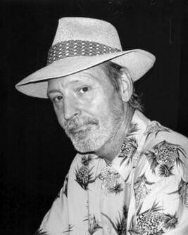 Man in a white hat and floral shirt, posing against a dark background.