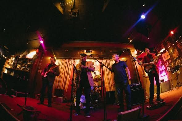 Band performing on a small stage under colorful lights in a dim club