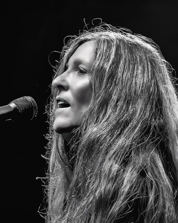 Black-and-white close-up of a singer with long hair performing into a microphone