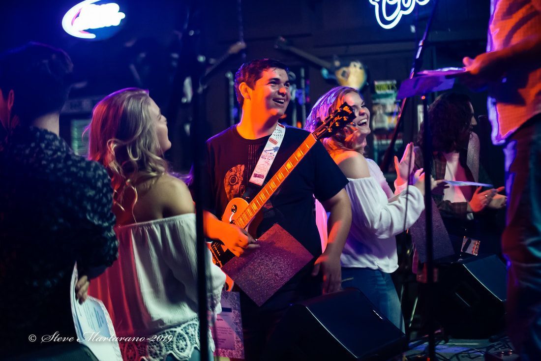 Band performing on a neon-lit stage as people dance in front of them.
