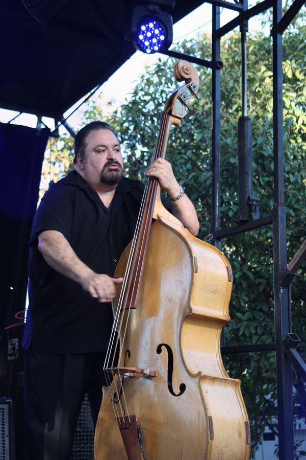 Musician playing an upright bass on an outdoor stage under blue lights