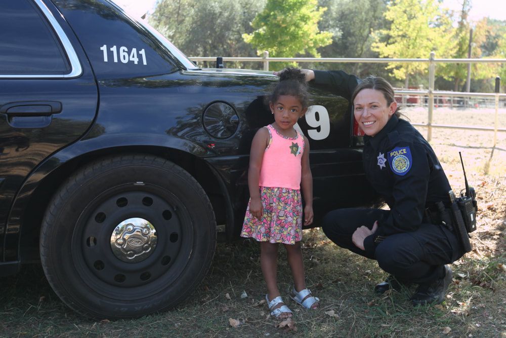 Police officer kneeling beside a child in front of a black police car outdoors