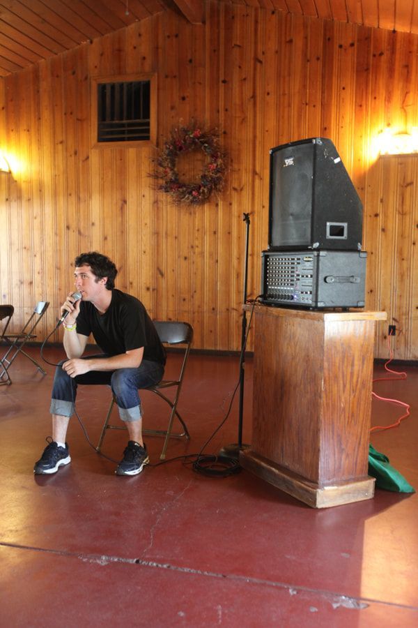 Person sitting on a chair in a wood-paneled hall beside a speaker on a podium