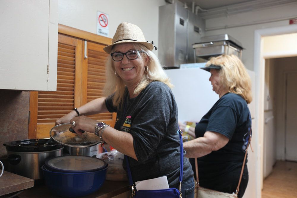 Two women cooking in a kitchen, one stirring a pot while smiling at the camera