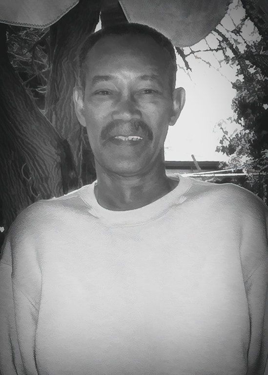 Portrait of a man in a white shirt standing outdoors near a tree, with a neutral expression.