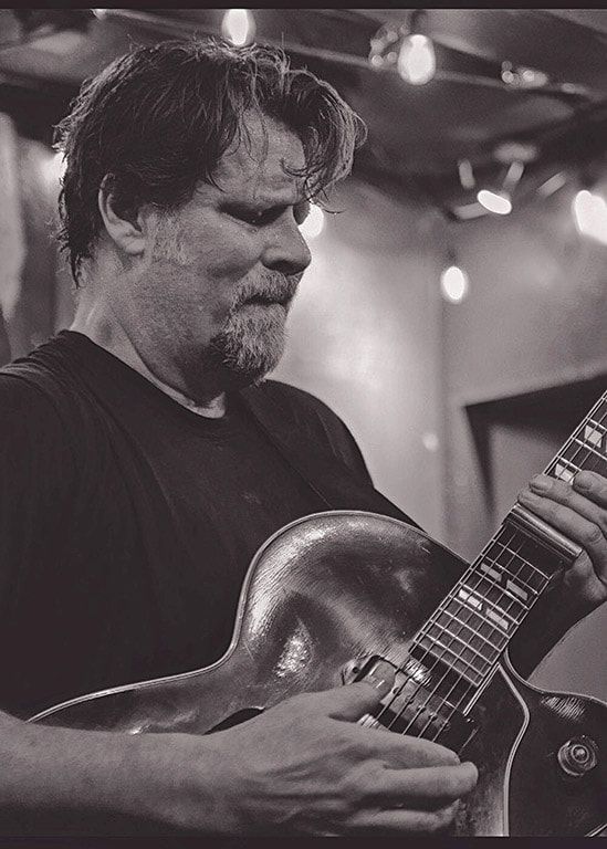 Black-and-white close-up of a guitarist playing an electric guitar on stage
