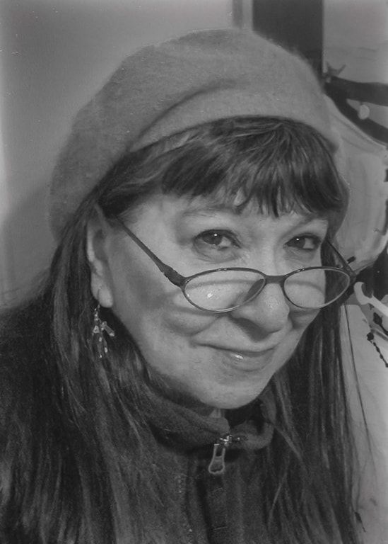 Close-up portrait of a smiling person wearing glasses and a knit hat, in black and white.