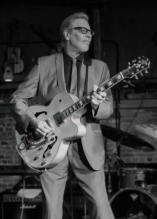 Man in suit playing an electric guitar onstage under dim lighting