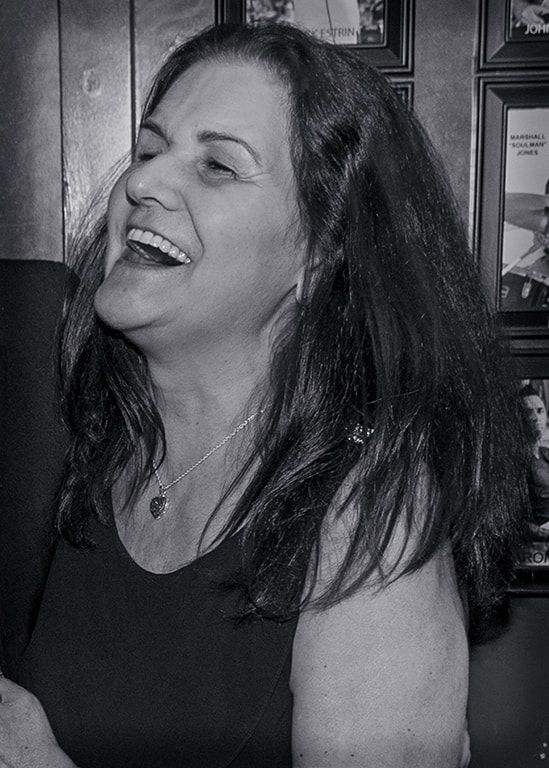 Woman laughing in a dark sleeveless top, shown in a black-and-white portrait.