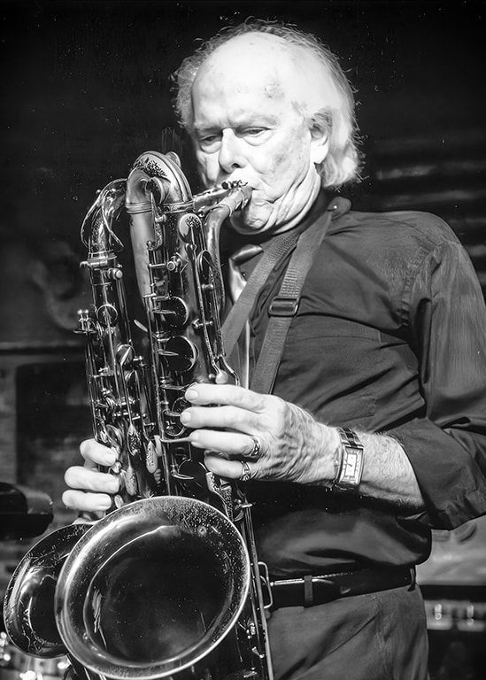Black-and-white photo of a musician playing a large saxophone on stage