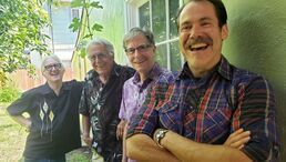 Four smiling people standing together outdoors by a window and greenery