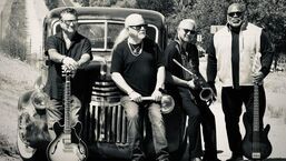 Four musicians posing with guitars in front of a vintage van outdoors