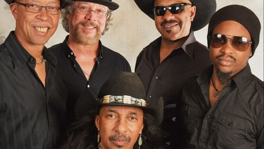 Five smiling men in black shirts pose together against a light background.