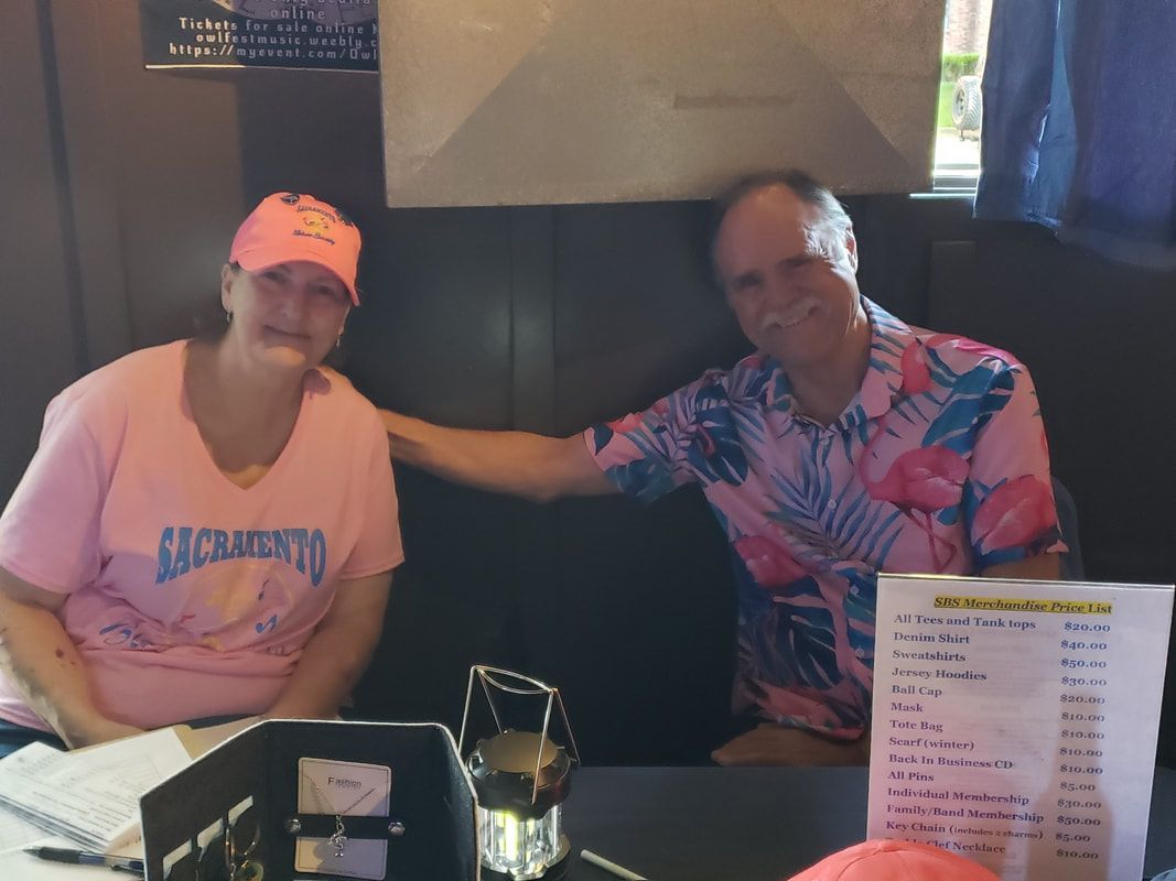 Two people sitting on a couch in a dim restaurant booth, one wearing a pink shirt and cap, the other a colorful shirt.
