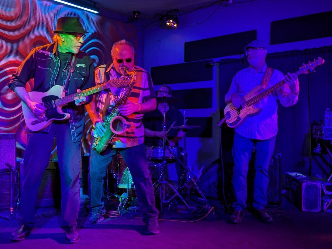 Four musicians performing onstage under colorful purple and blue lights, with guitars and saxophone.