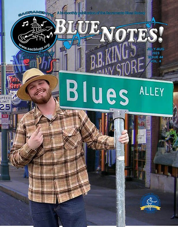 Man posing by a green “Blues Alley” street sign in front of a Blues Notes music store.