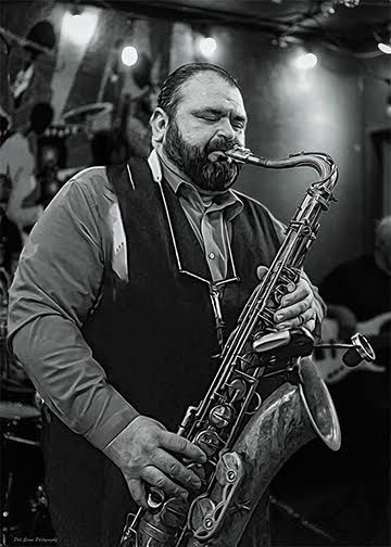 Black-and-white photo of a saxophonist playing on stage under bright lights