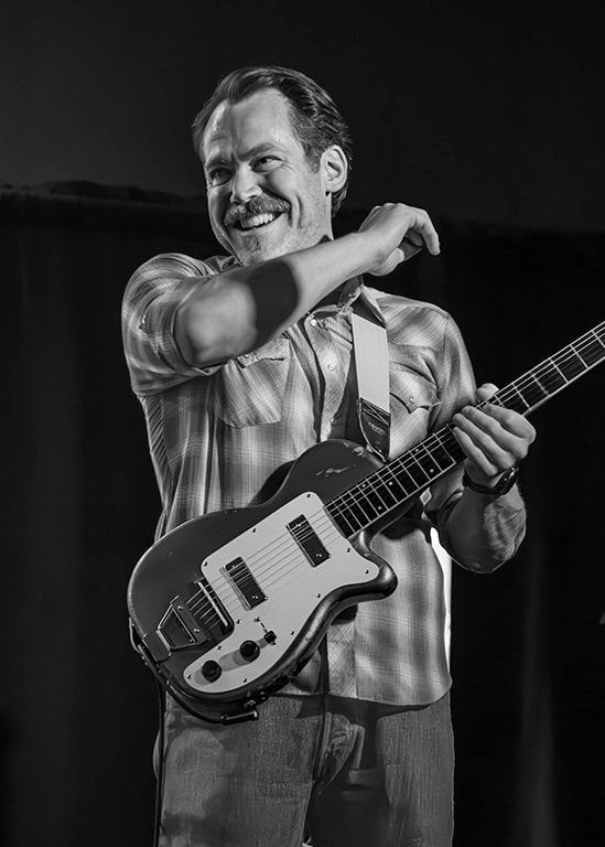 Black-and-white photo of a smiling musician holding an electric guitar onstage