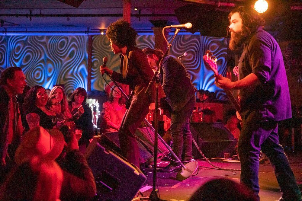 Live band performing on a colorful stage with red lighting and an audience watching closely