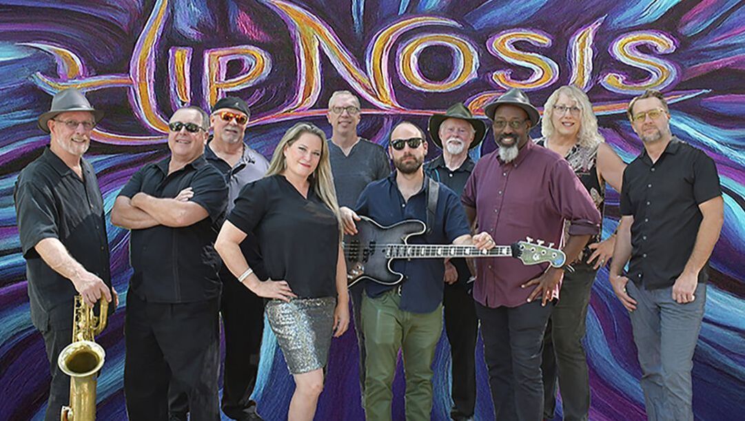 Group of musicians posing in front of a colorful “HYPNOSIS” mural, holding instruments and smiling