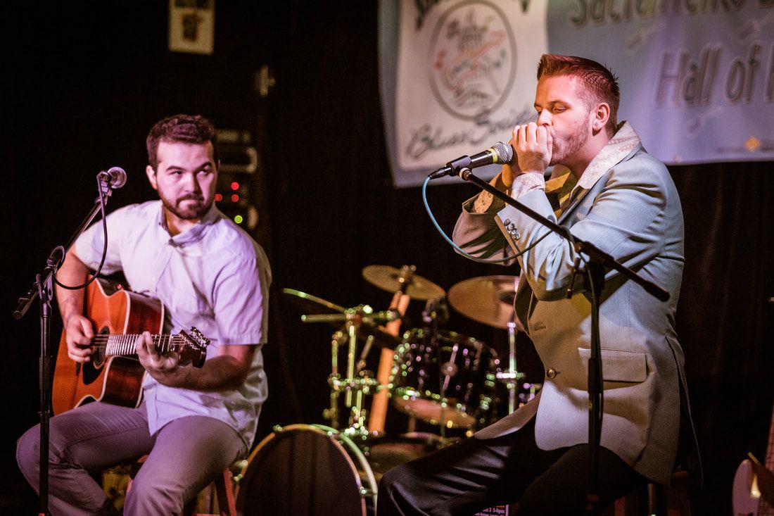 Two musicians performing on stage, one playing guitar and one singing into a microphone.