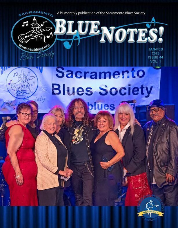 People posing on a stage in front of a Sacramento Blues Society Blue Notes! backdrop