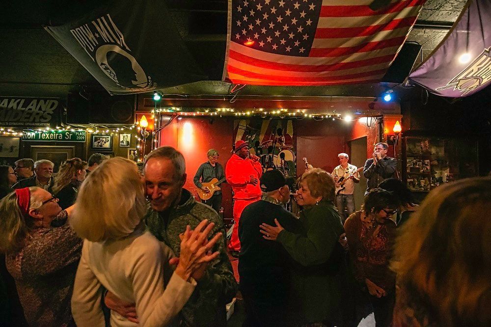 People dancing in a dimly lit bar with a live band on stage and American flags overhead