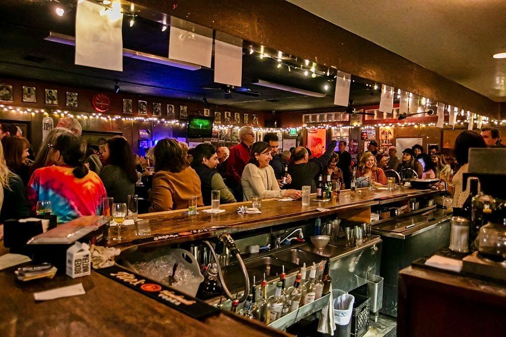 Crowded bar with patrons seated at a long counter under warm ambient lighting
