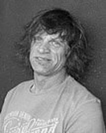 Grayscale portrait of a person with long hair wearing a T-shirt, looking toward the camera with a slight smile