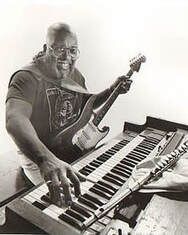 Person playing a keyboard while holding a guitar, with sheet music on the stand.