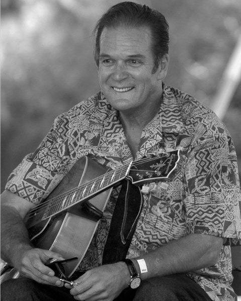 Smiling man in patterned shirt holding a guitar outdoors
