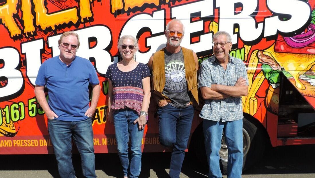 Four people standing in front of a colorful truck mural, posing with arms around each other