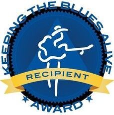 Blue circular award badge with yellow ribbon reading “Recipient” and text “Keeping the Blues Alive Award”