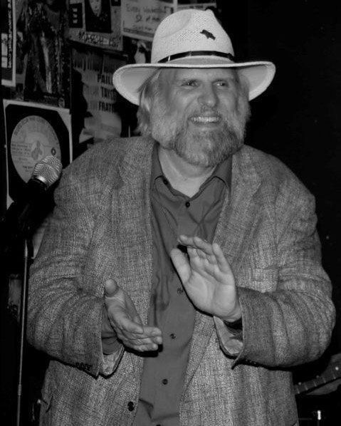 Man in a white hat smiling and clapping in a dimly lit room