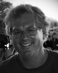 Smiling person with glasses in a black-and-white portrait, with blurred flowers in the background