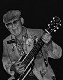Man in a cap playing a banjo on a dark stage, focused expression