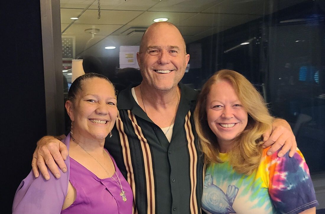Three smiling people posing indoors, with arms around each other.