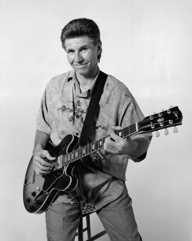 Man playing an electric guitar, smiling in a studio setting.