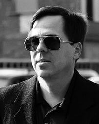 Black-and-white portrait of a man wearing sunglasses and a dark coat outdoors