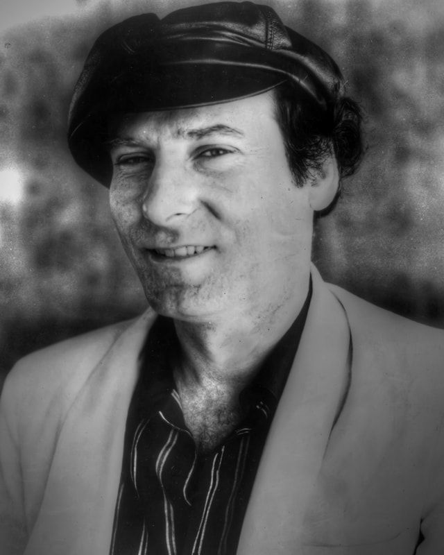 Black-and-white portrait of a person wearing a cap and light jacket, looking at the camera with a slight smile.