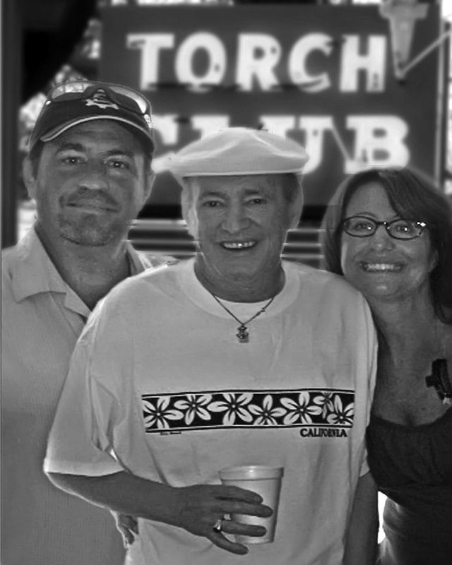 Three smiling people posing in front of a Torch Club sign, one holding a drink